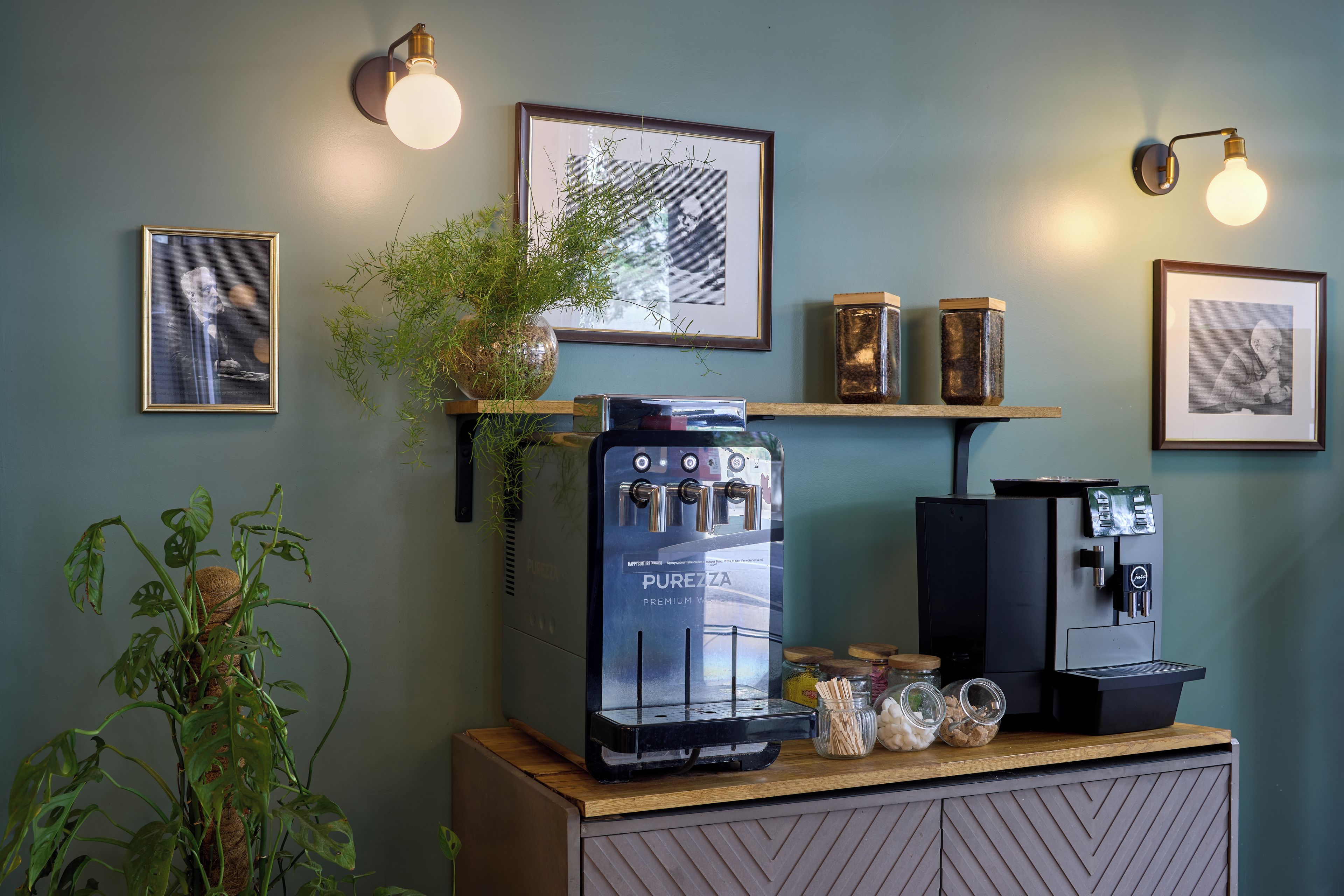 Eine Kaffeebar mit einer Purozza-Espressomaschine, zwei wandmontierten Kaffeeausgabegeräten und gerahmten Kunstwerken an der Wand.