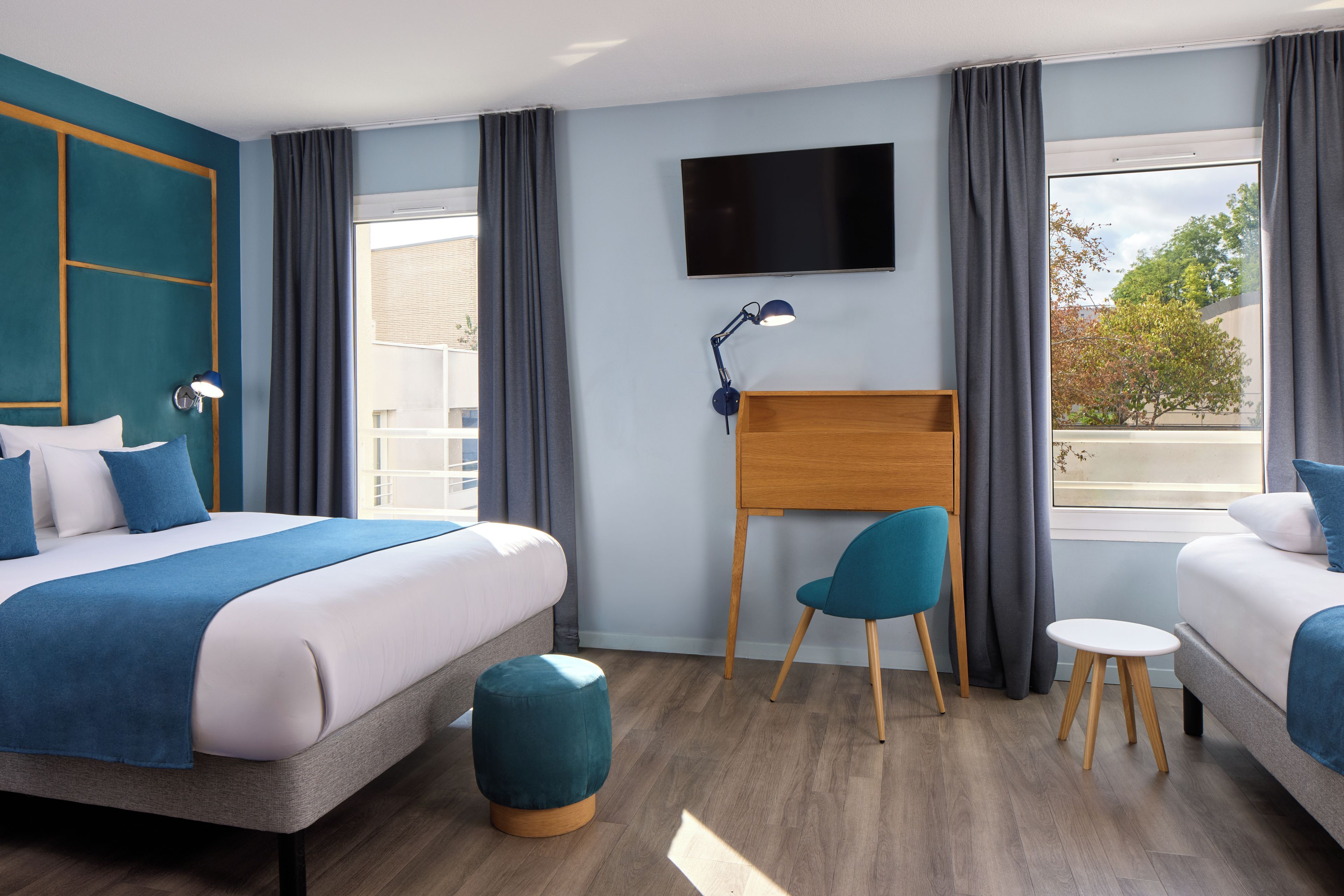 Ein Hotelzimmer mit Bett, Schreibtisch, Stuhl, Fernseher und einem Fenster mit Vorhängen.
