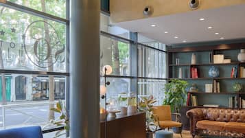 A modern interior with a large window, a round glass table, a leather sofa, and a bookshelf.