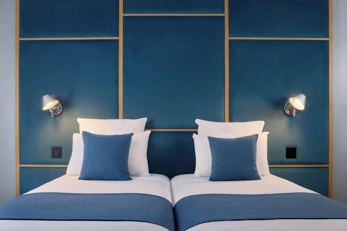 A double bed with two pillows, a headboard with a geometric design, and wall-mounted lighting.