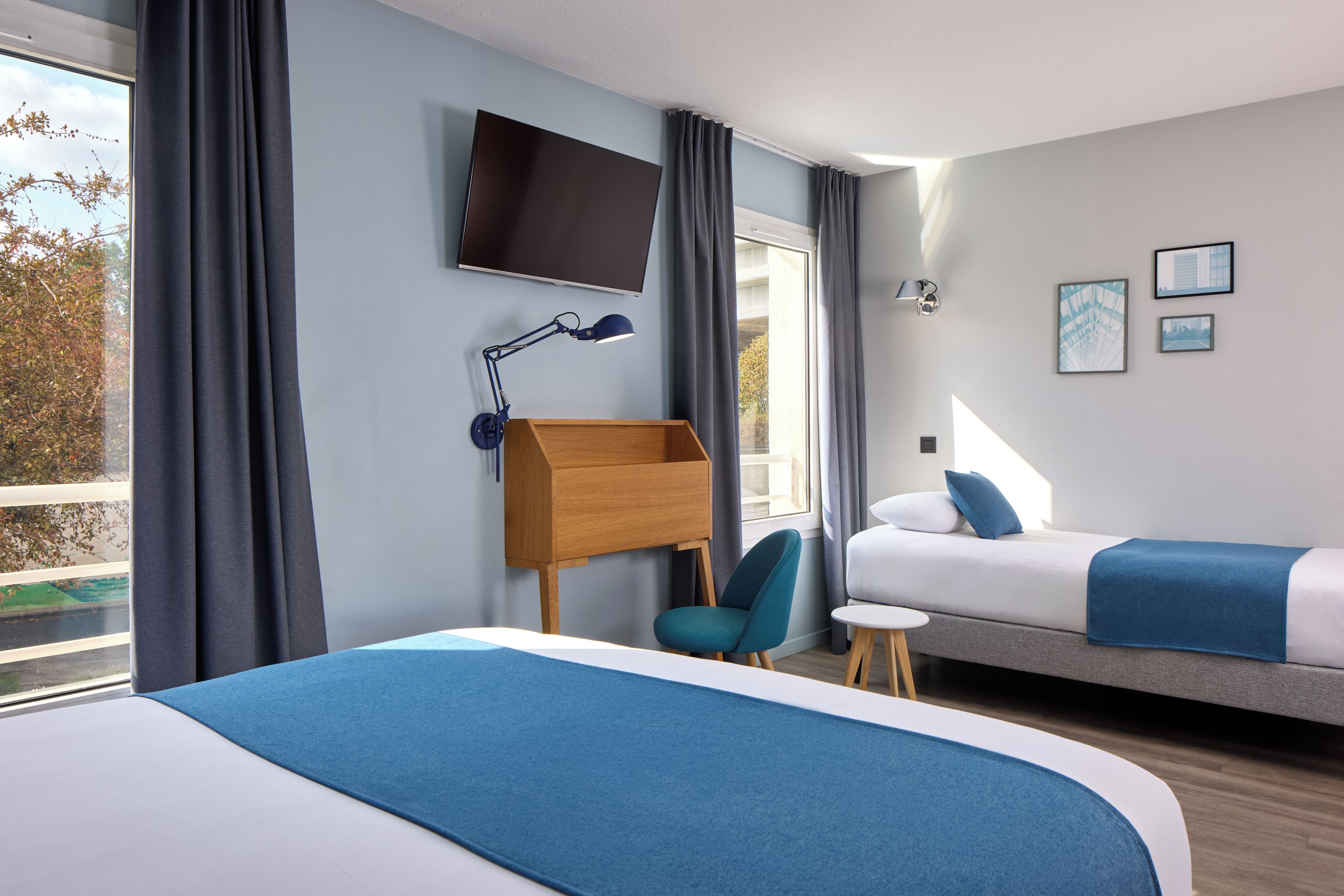 Ein Hotelzimmer mit Bett, Schreibtisch mit Stuhl, Wandfernseher und einem Fenster mit Vorhängen.