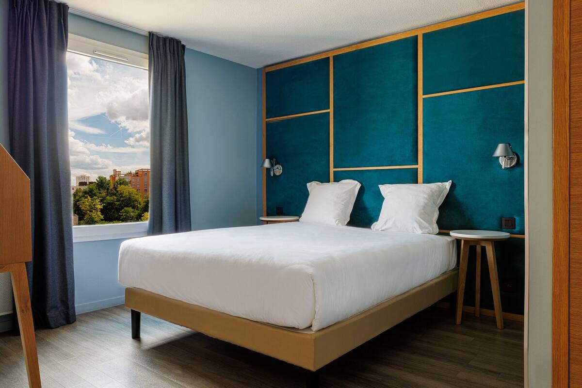 Une chambre d’hôtel moderne avec un grand lit, une vue sur la ville et une fenêtre avec des rideaux.