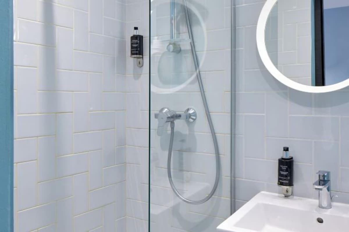 A bathroom with a glass-enclosed shower, a white sink, and a round mirror.