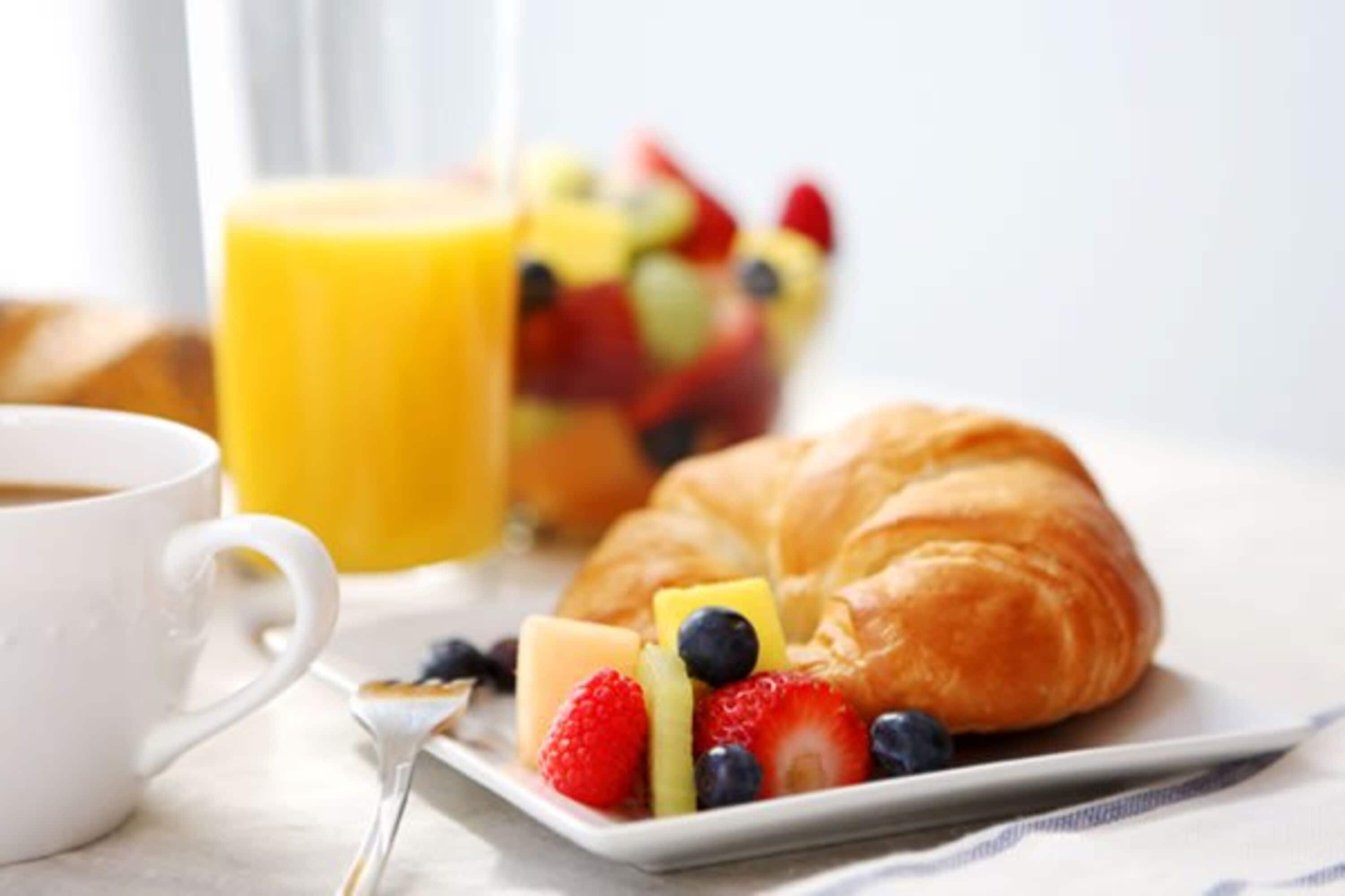 A breakfast setting with a croissant, fruit, and a glass of orange juice.