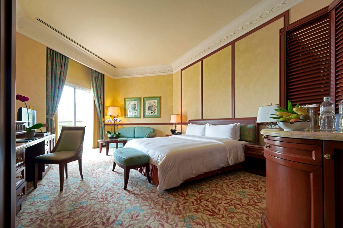 Habitación de hotel con cama, escritorio, silla y una mesita de noche con lámpara.