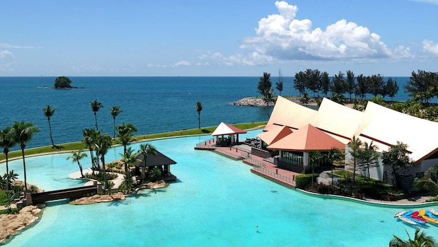 A resort with a large swimming pool, beach views, and palm trees.