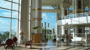 A spacious lobby with large windows, a grand staircase, and a view of the ocean.