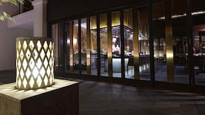 A modern building exterior with a large, illuminated decorative column and a view into a restaurant area with a chef visible.