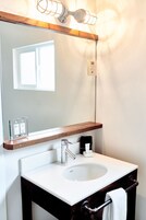 Un baño con lavamanos blanco, encimera de madera y un espejo encima. Hay un perchero y un dispensador de jabón en la encimera.