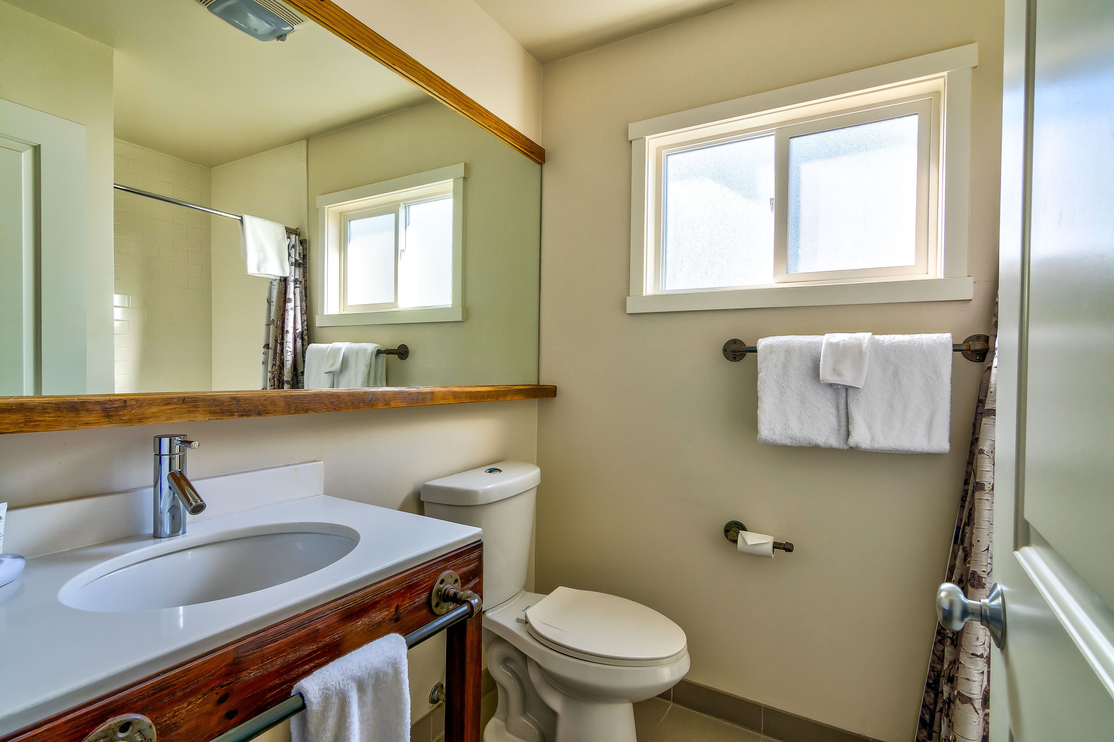 A bathroom with a sink, toilet, and a window above the toilet.