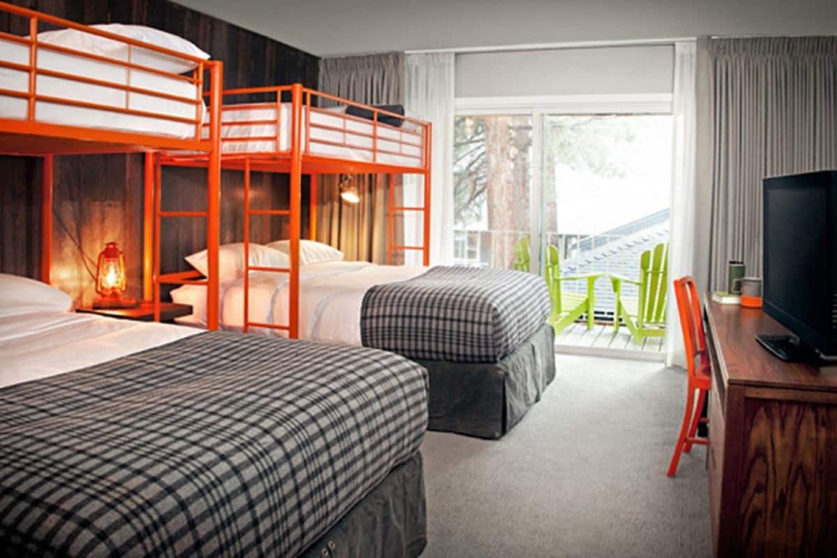 A hotel room with two beds, a desk with a TV, and a balcony with chairs.
