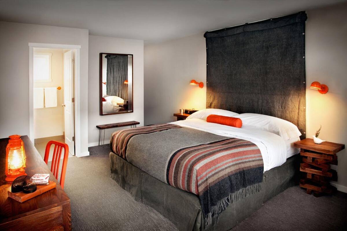 A bedroom with a large bed, a bedside table, a nightstand, a mirror, a chair, and a small table with a lantern.
