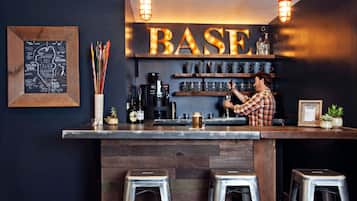 Un espace bar avec un comptoir en bois, des tabourets en métal et une enseigne sur laquelle on peut lire « BASE ».