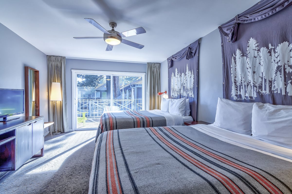 A hotel room with a bed, a ceiling fan, a TV, and a view of the outdoors.