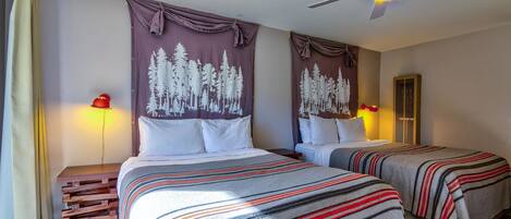 A hotel room with two beds, a ceiling fan, and a nightstand with a lamp.