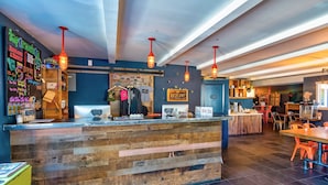 Un mostrador de recepción de madera con un menú en una pizarra, luces colgantes y un letrero que dice 'BASE CAMP'.