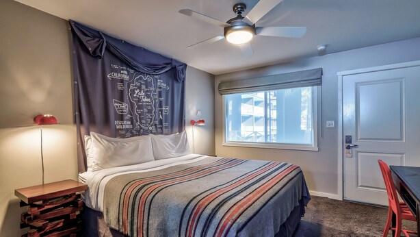 A bedroom with a bed, a ceiling fan, a window, and a door. - Basecamp South Lake Tahoe (South Lake Tahoe)