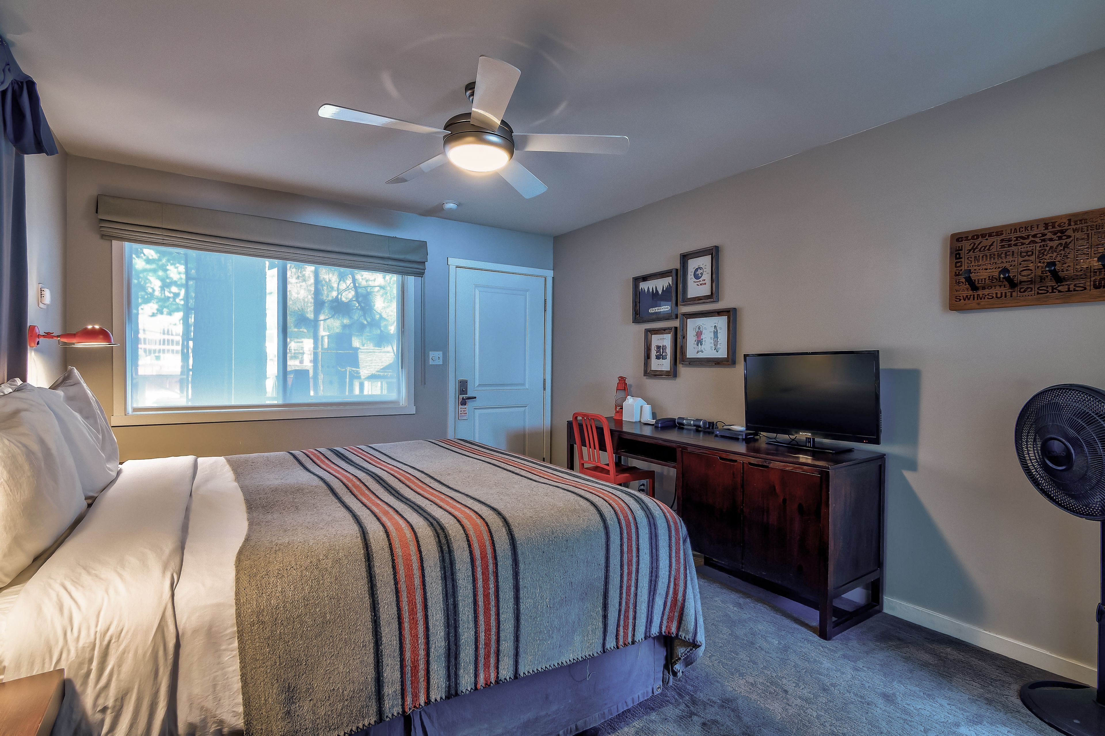 A bedroom with a bed, a desk, a TV, and a ceiling fan.