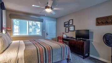 A bedroom with a bed, a desk, a TV, and a ceiling fan.