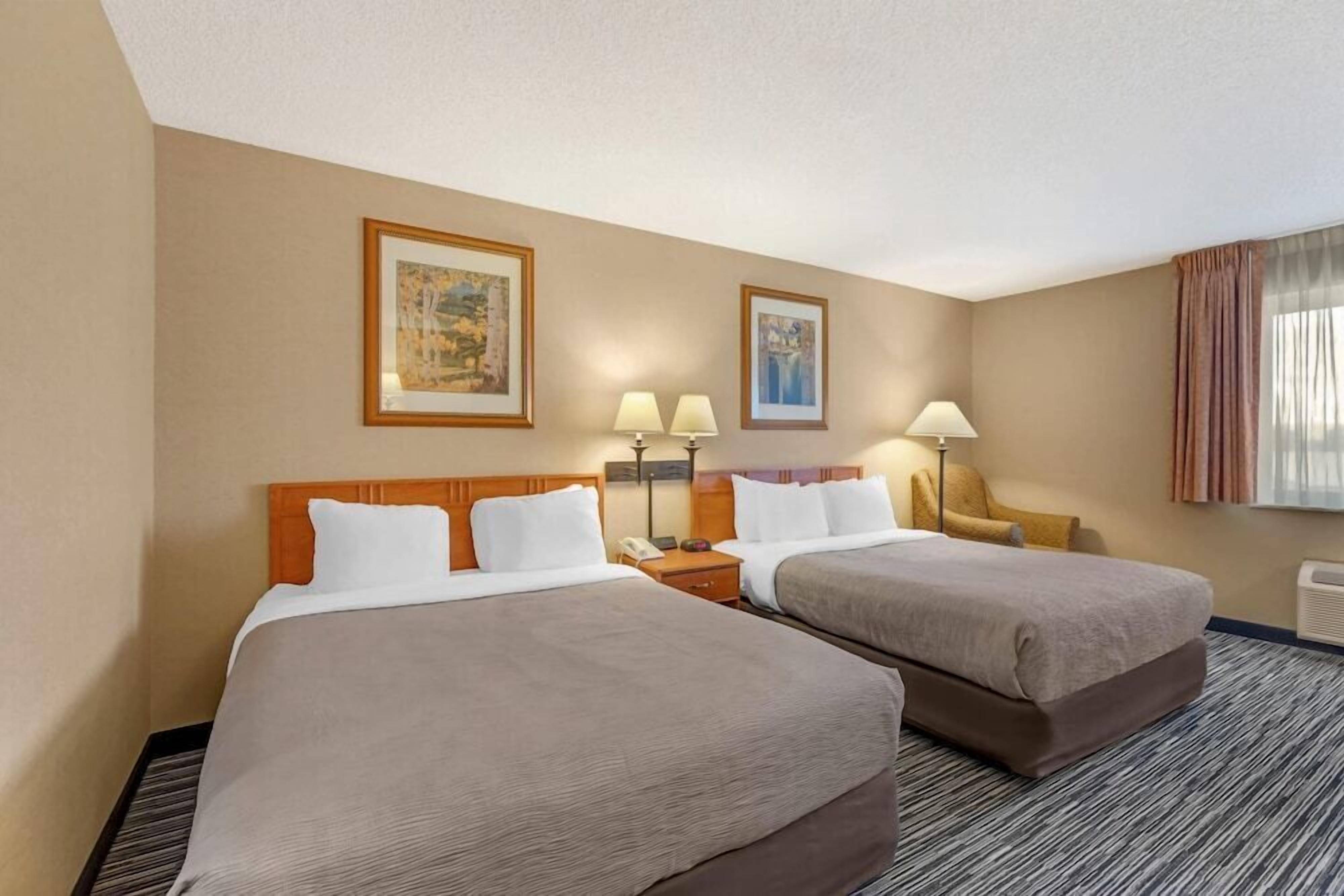 A hotel room with two beds, a nightstand, lamps, and framed artwork on the wall.