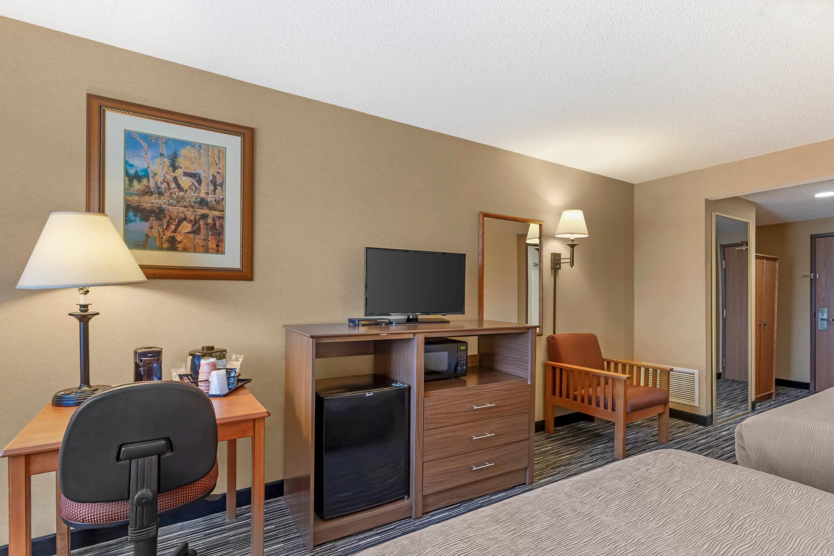 A hotel room with a desk, chair, television, microwave, refrigerator, and a bed.