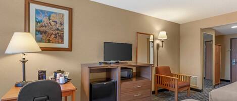 A hotel room with a desk, chair, television, microwave, refrigerator, and a bed.