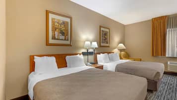 Une chambre d’hôtel avec deux lits, une tête de lit en bois, deux tables de chevet avec des lampes et deux tableaux encadrés au mur.