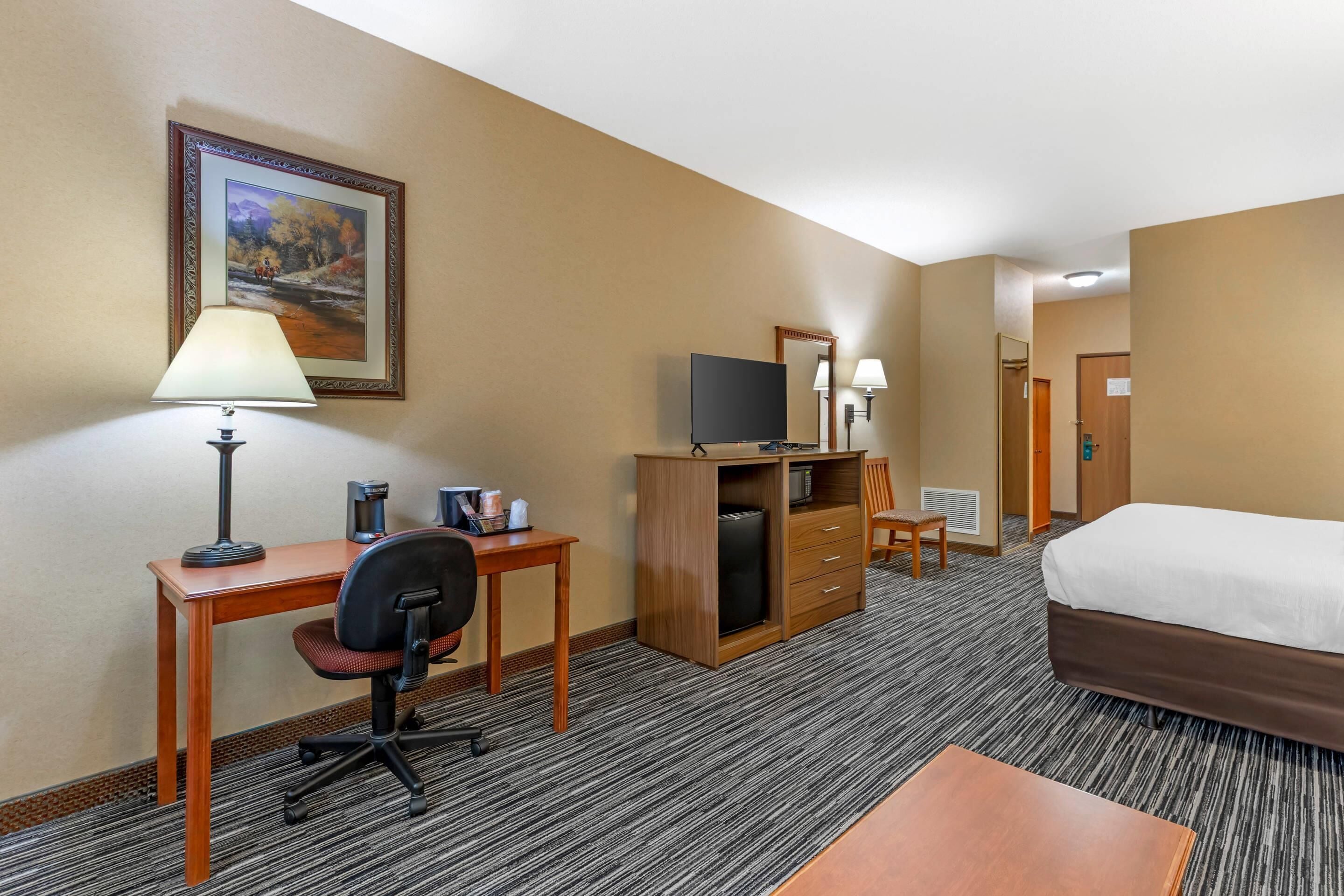 A hotel room with a bed, desk, chair, TV, dresser, and a painting on the wall.