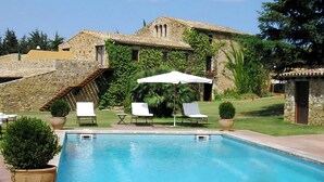 A pool area with lounge chairs and umbrellas, a stone building with ivy, and a clear sky. - Mas Salvi Country Boutique Hotel (Pals)