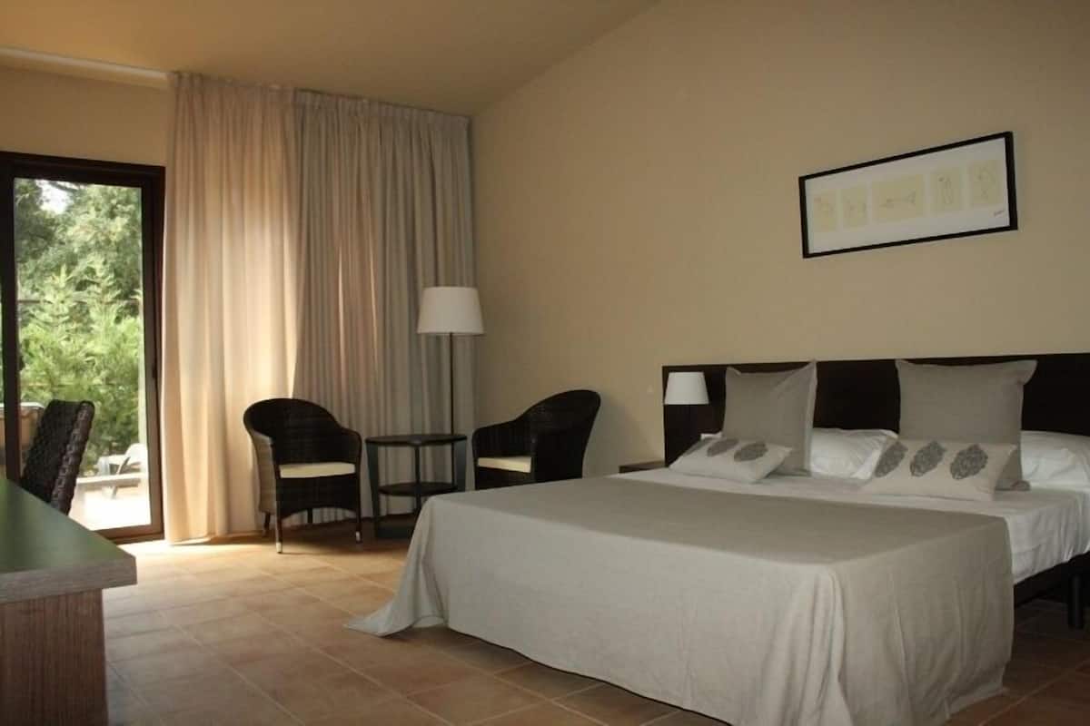 A hotel room with a bed, two chairs, a small table, and a window with curtains.