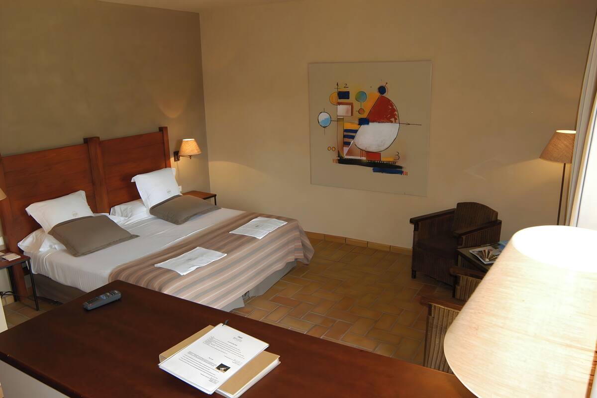 A hotel room with a bed, a desk, a lamp, and a wall art piece.