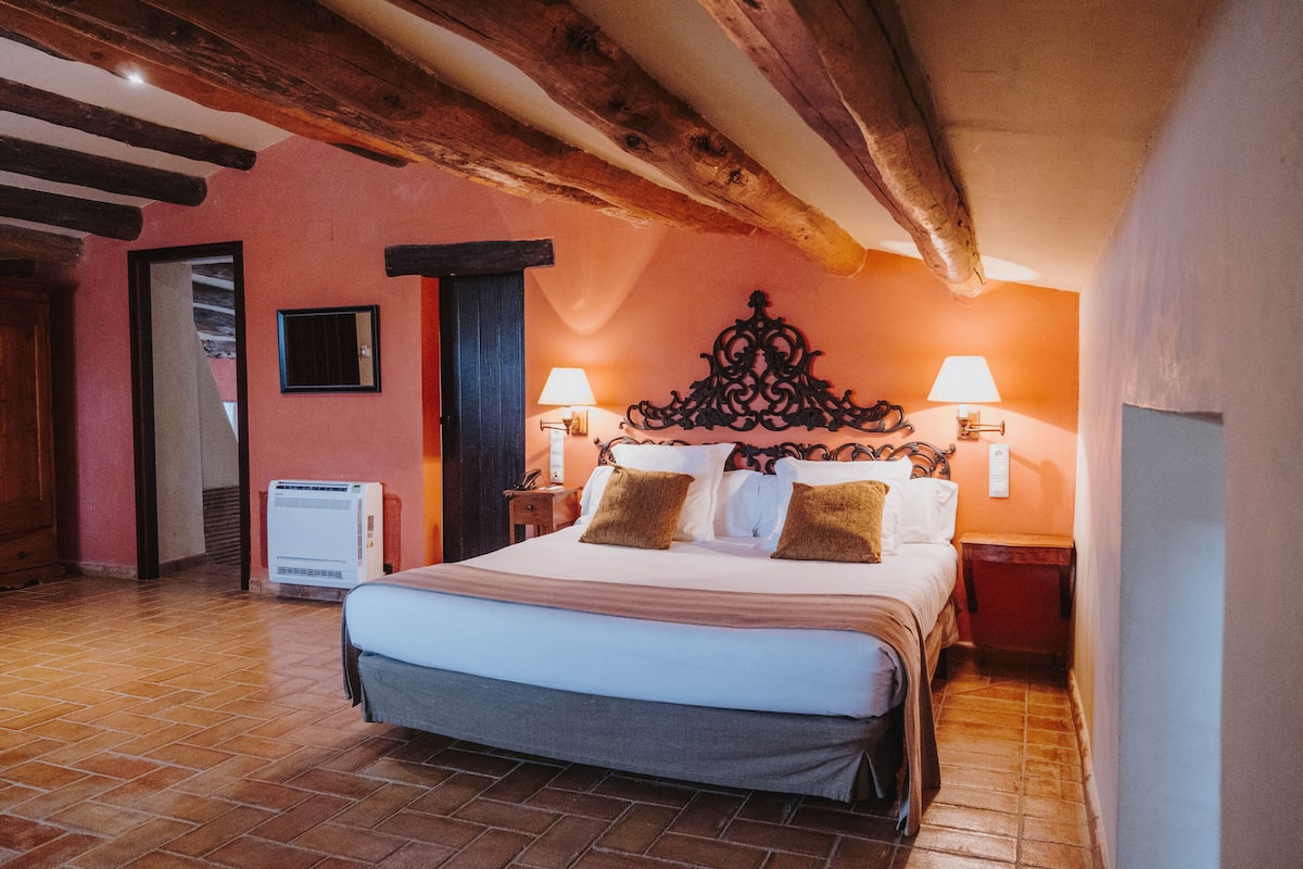 A hotel room with a large bed, two bedside lamps, a wooden headboard, and a tiled floor.