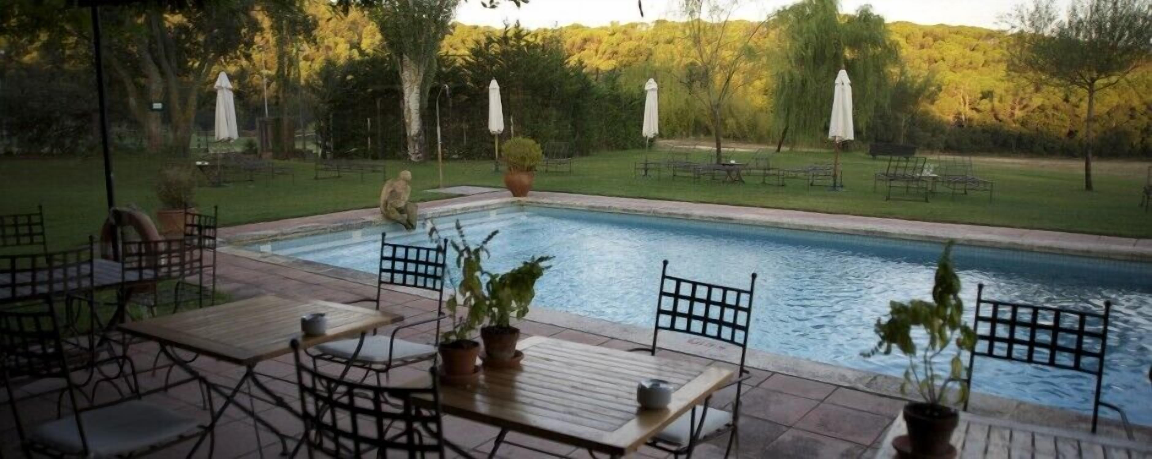 An outdoor swimming pool with a patio area, surrounded by trees and umbrellas.