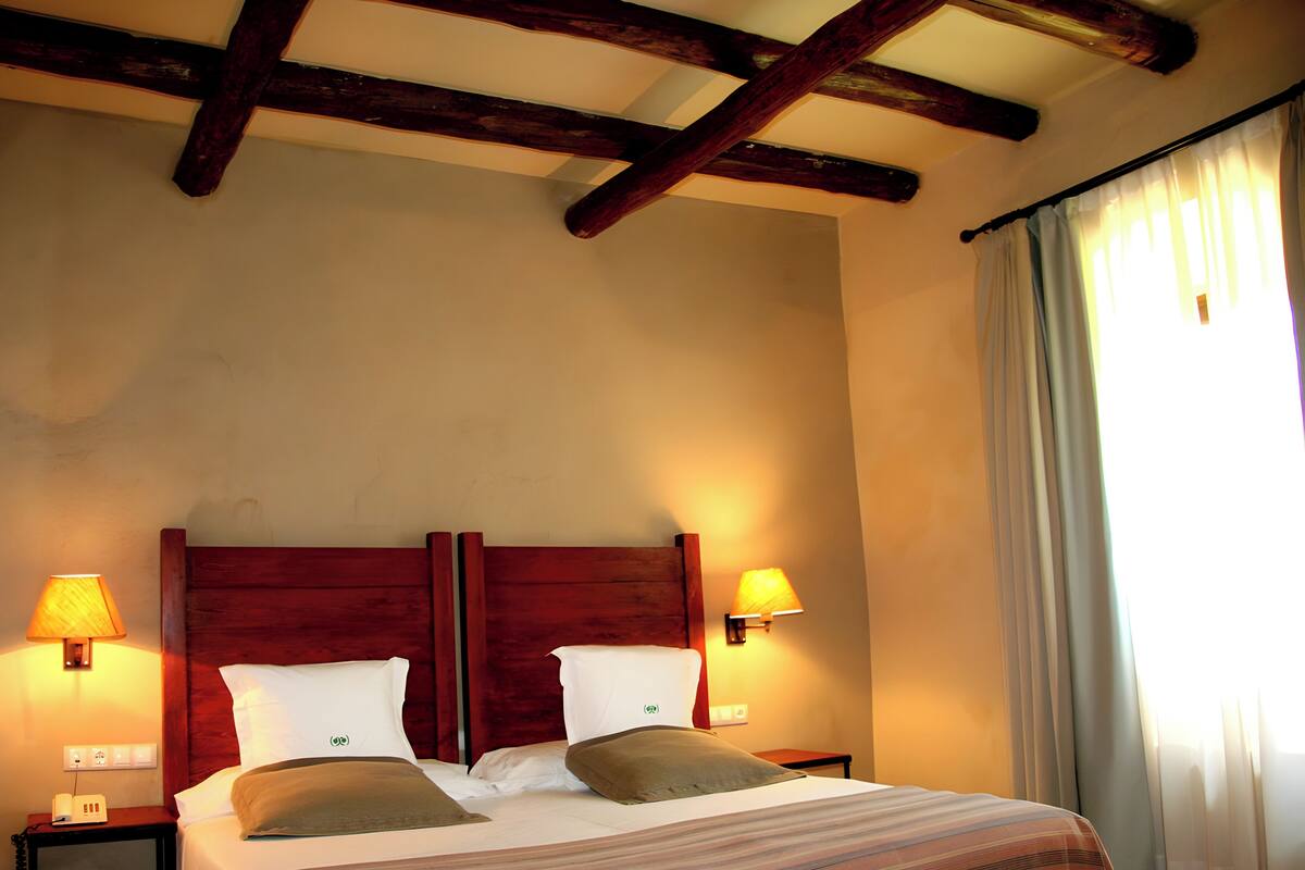 A hotel room with a wooden headboard, two bedside lamps, a bed with striped bedding, and a window with curtains.
