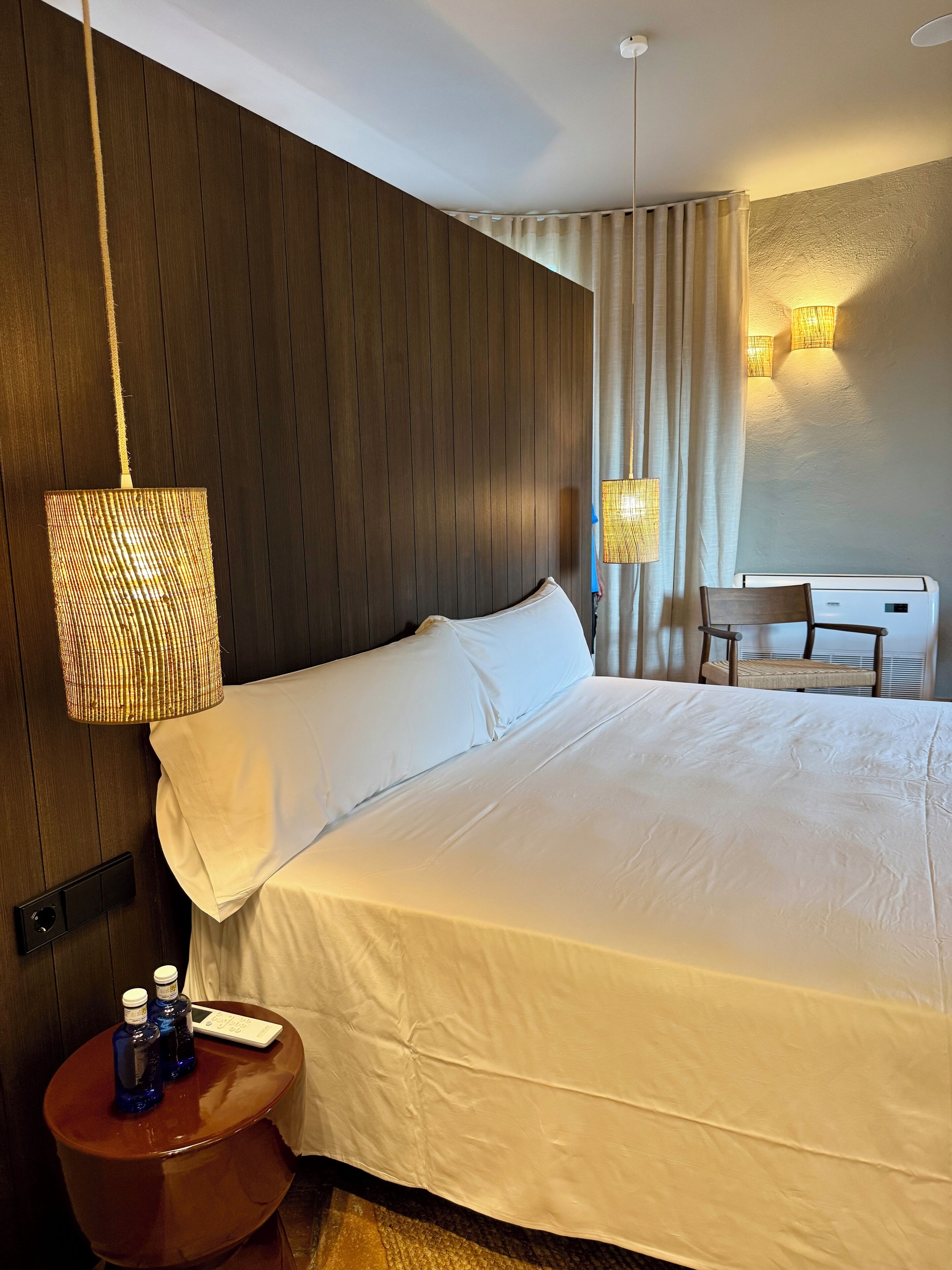 Habitación de hotel con una cama grande, una mesita de noche con dos botellas, una silla y un escritorio con una computadora.