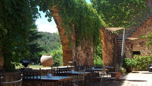 An outdoor patio with stone tables and chairs, surrounded by greenery and a stone wall. - Mas Salvi Country Boutique Hotel (Pals)