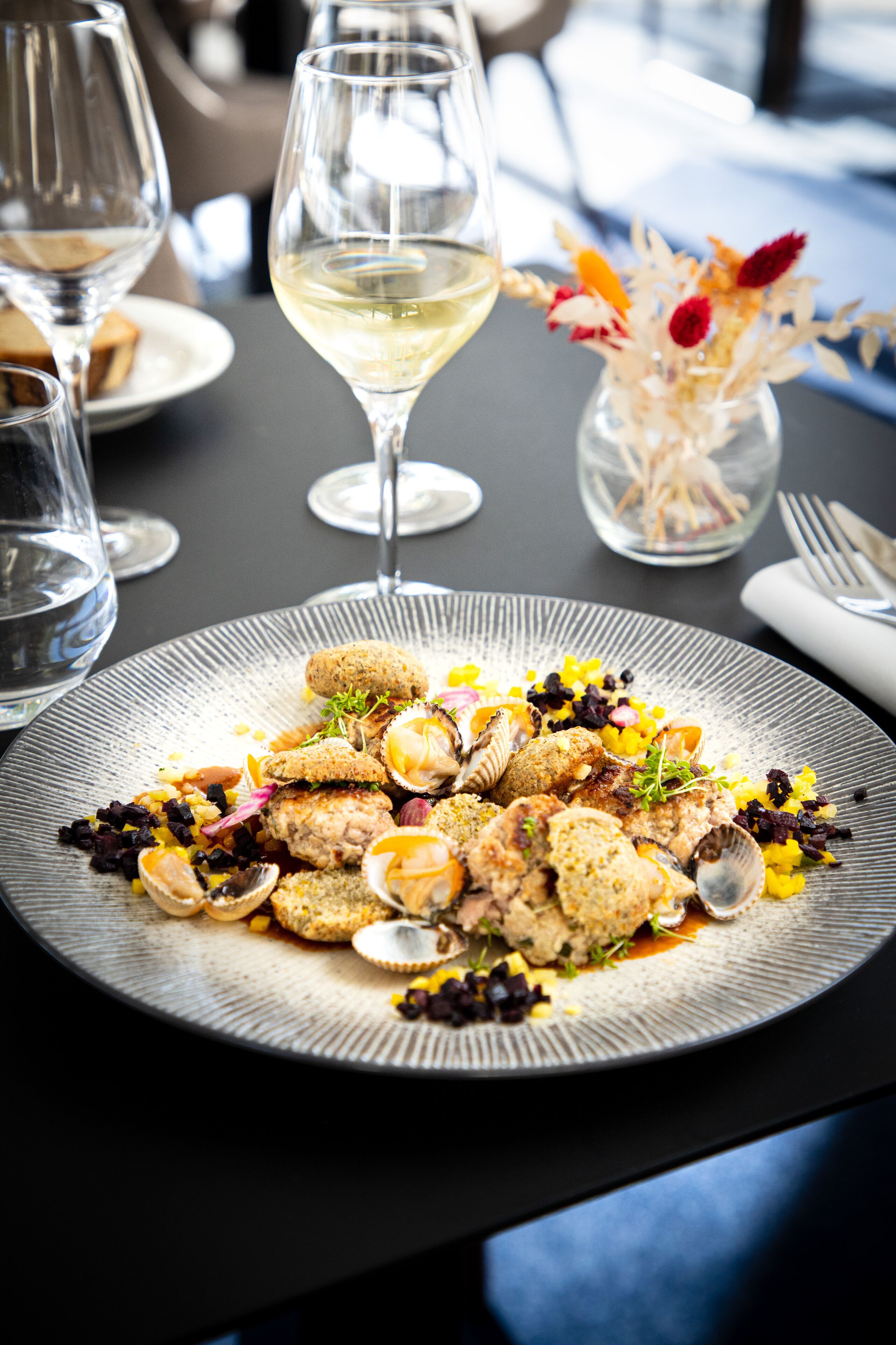 Una mesa de comedor con un plato de mariscos, copas de vino y un florero con flores.