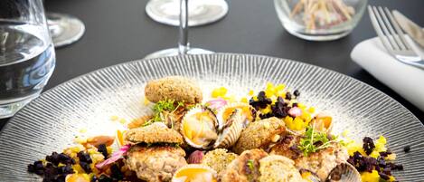 Una mesa de comedor con un plato de mariscos, copas de vino y un florero con flores.