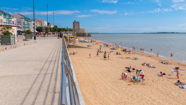 Una playa con paseo marítimo, sombrillas y gente relajándose.