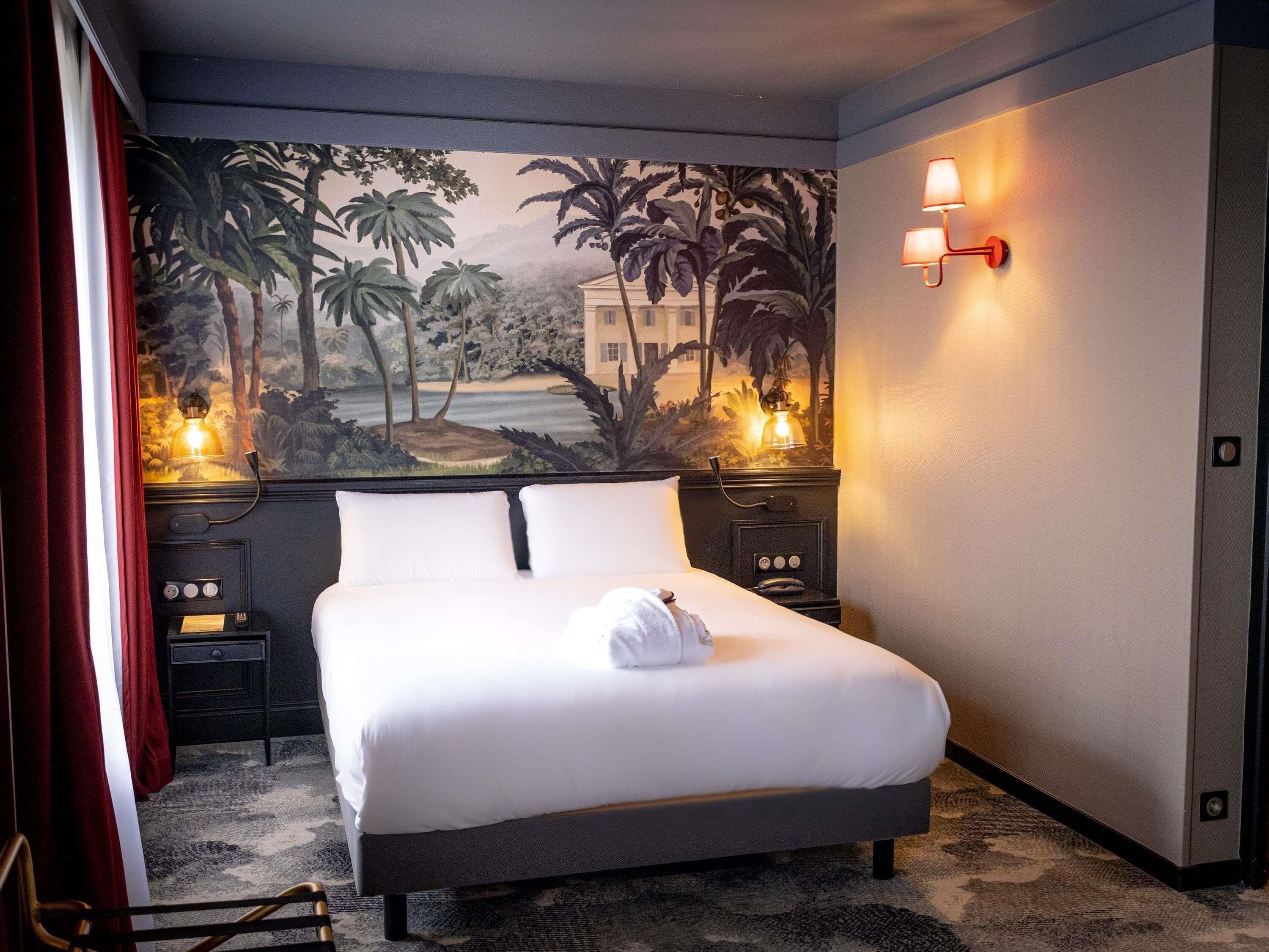 Una habitación de hotel con una cama, una mesita de noche, una lámpara y un mural en la pared.