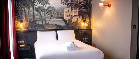 Una habitación de hotel con una cama, una mesita de noche, una lámpara y un mural en la pared.