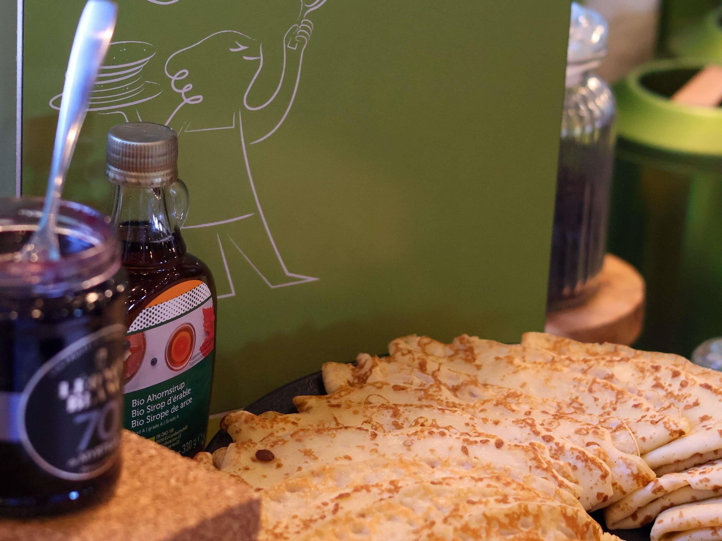 Una mesa con una botella de sirope, un dibujo de una persona y una pila de tortitas.