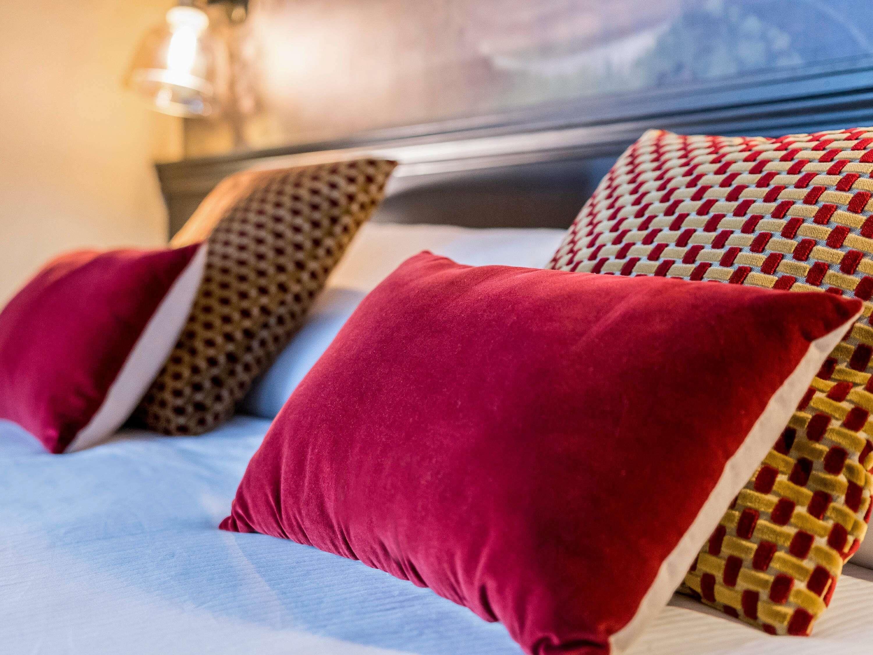 Una cama con múltiples almohadas, un cabecero y una mesita de noche con una lámpara.