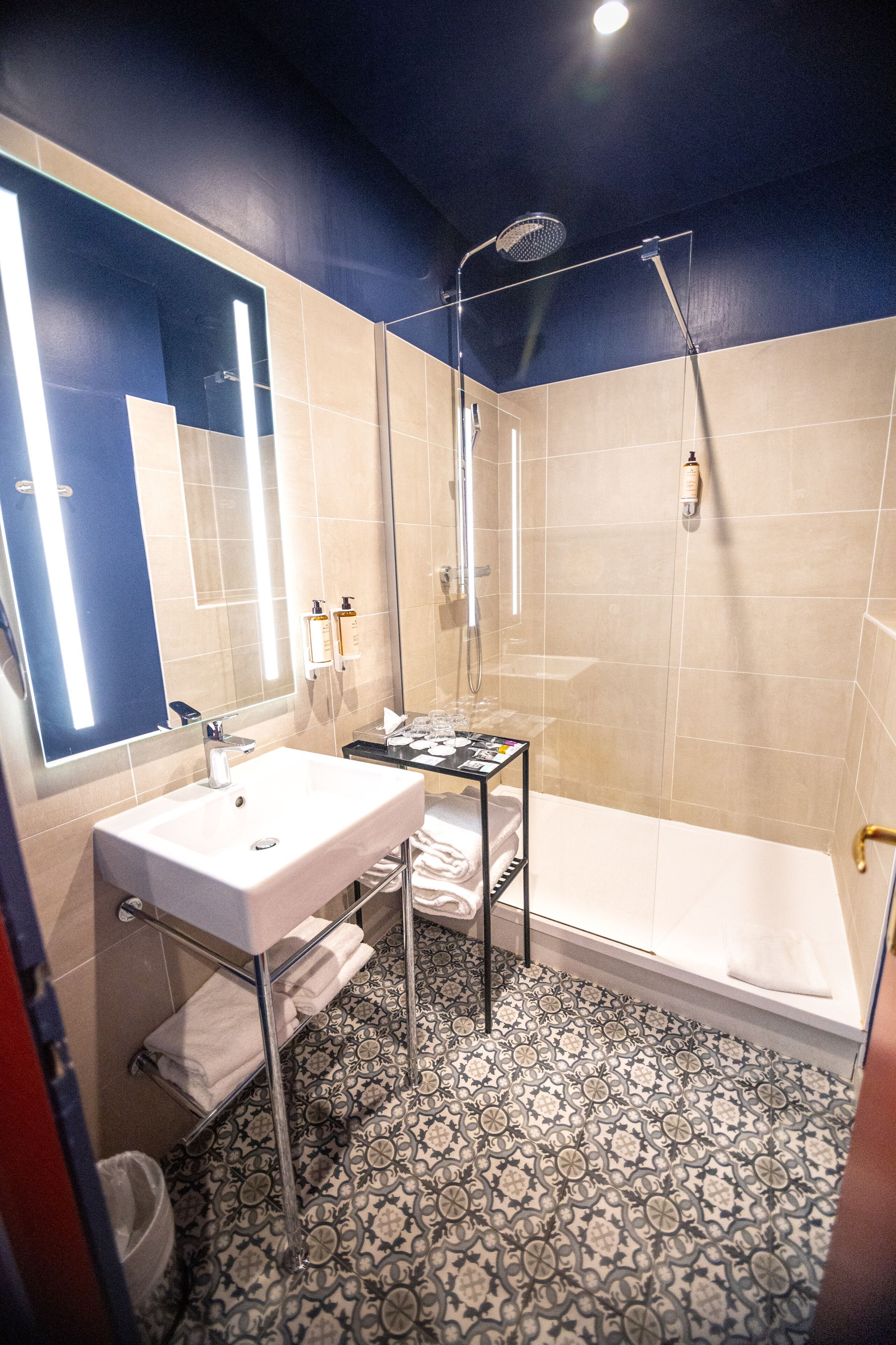 Un baño con lavamanos, espejo, ducha y baldosas de suelo estampadas.