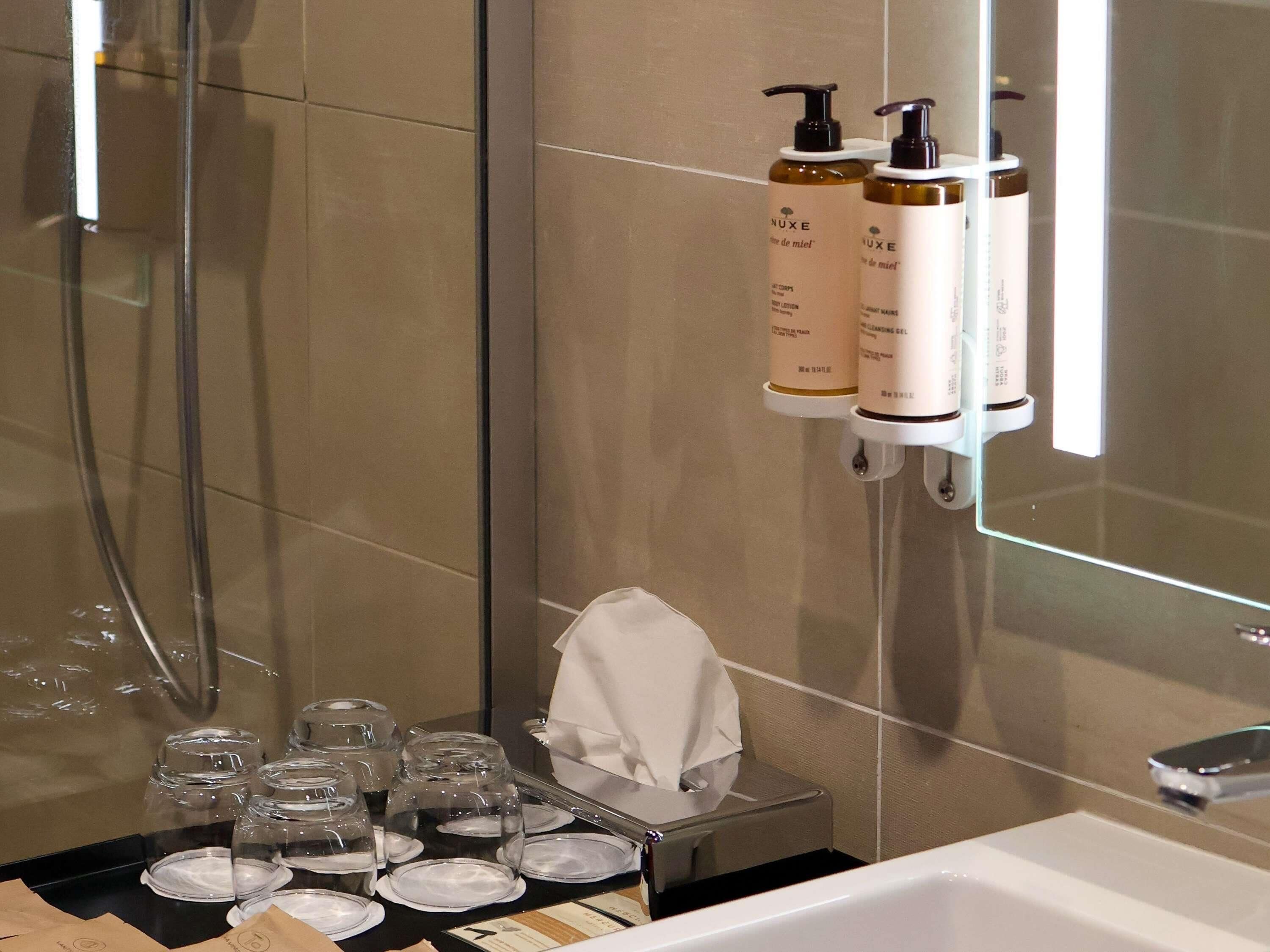 Un baño con cabina de ducha de vidrio, un lavabo con espejo y artículos de aseo en un estante.
