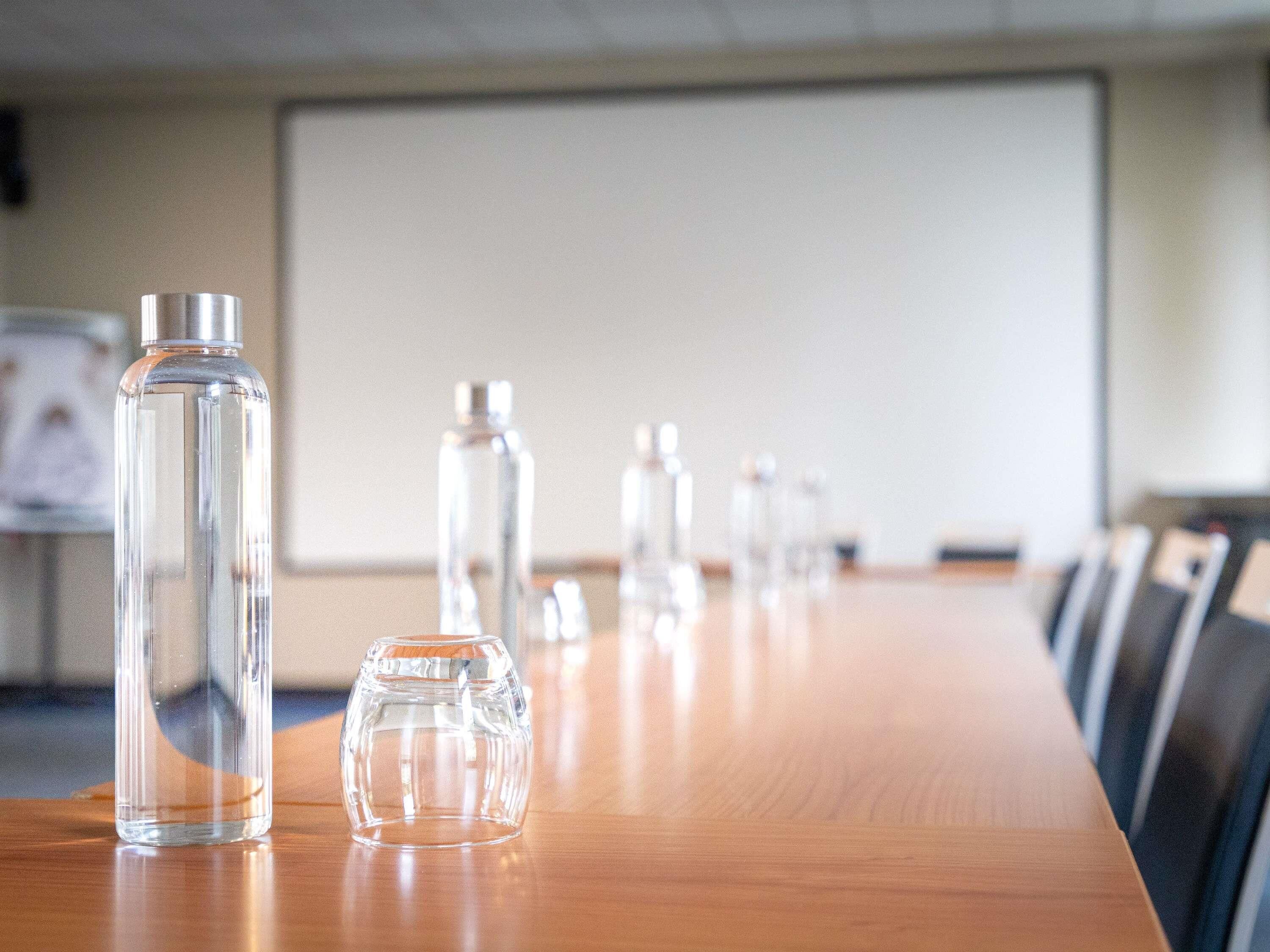 Une salle de conférence avec une longue table en bois et plusieurs bouteilles en verre transparent.