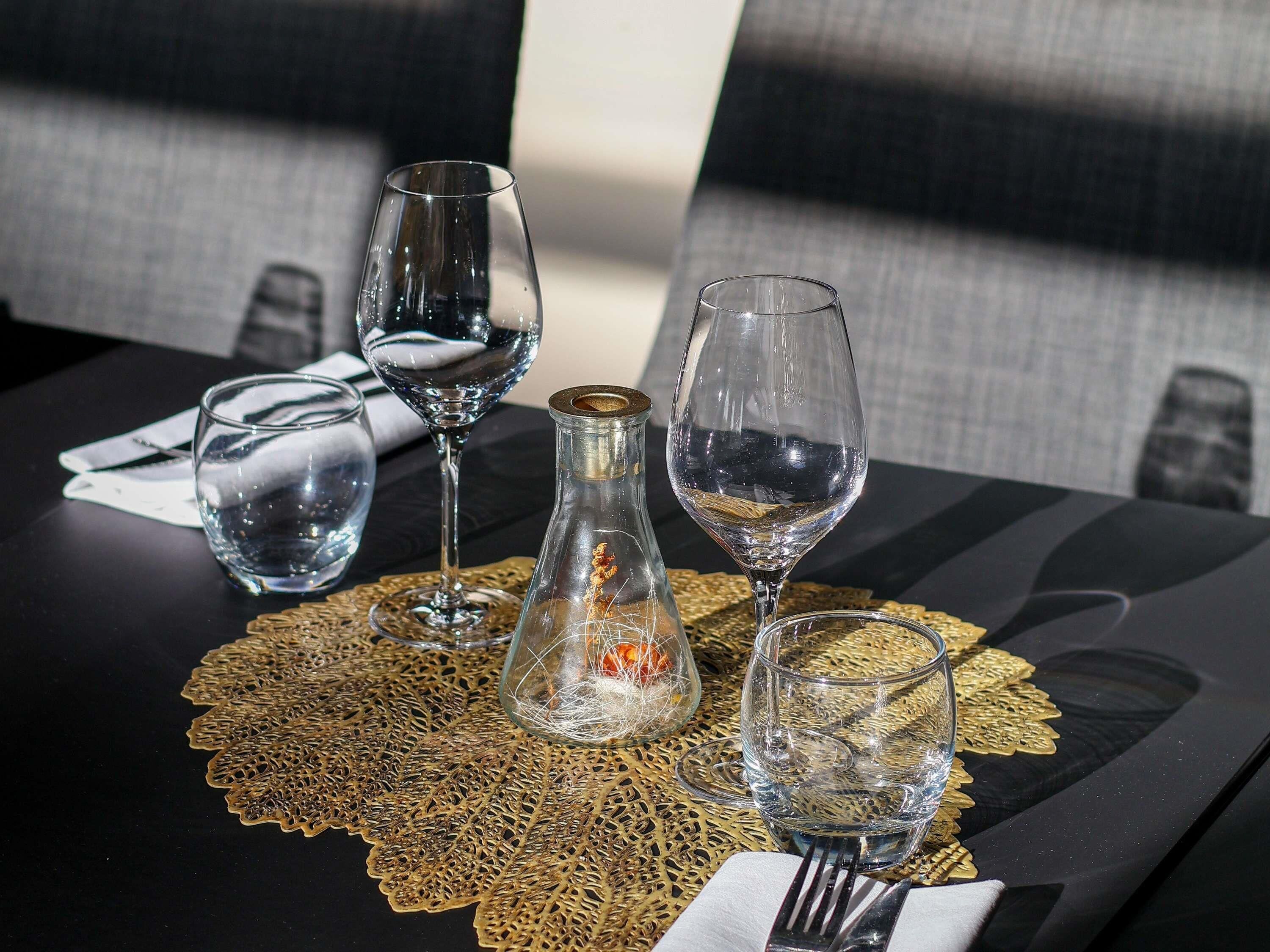 A dining table with four wine glasses, a glass bottle, and a gold-patterned placemat.