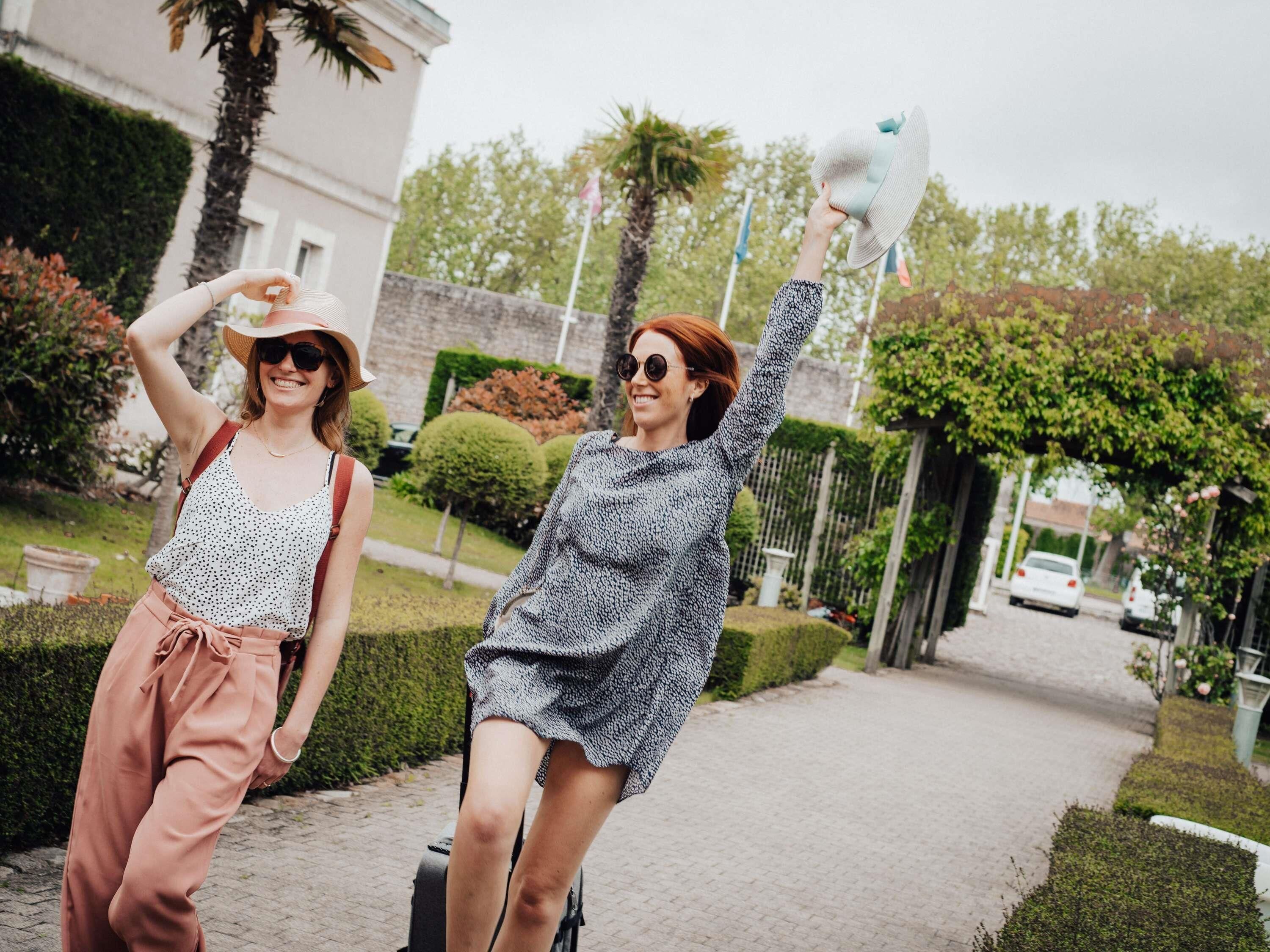 Twee personen wandelen over een geplaveid pad, met begroeiing en een gebouw op de achtergrond.