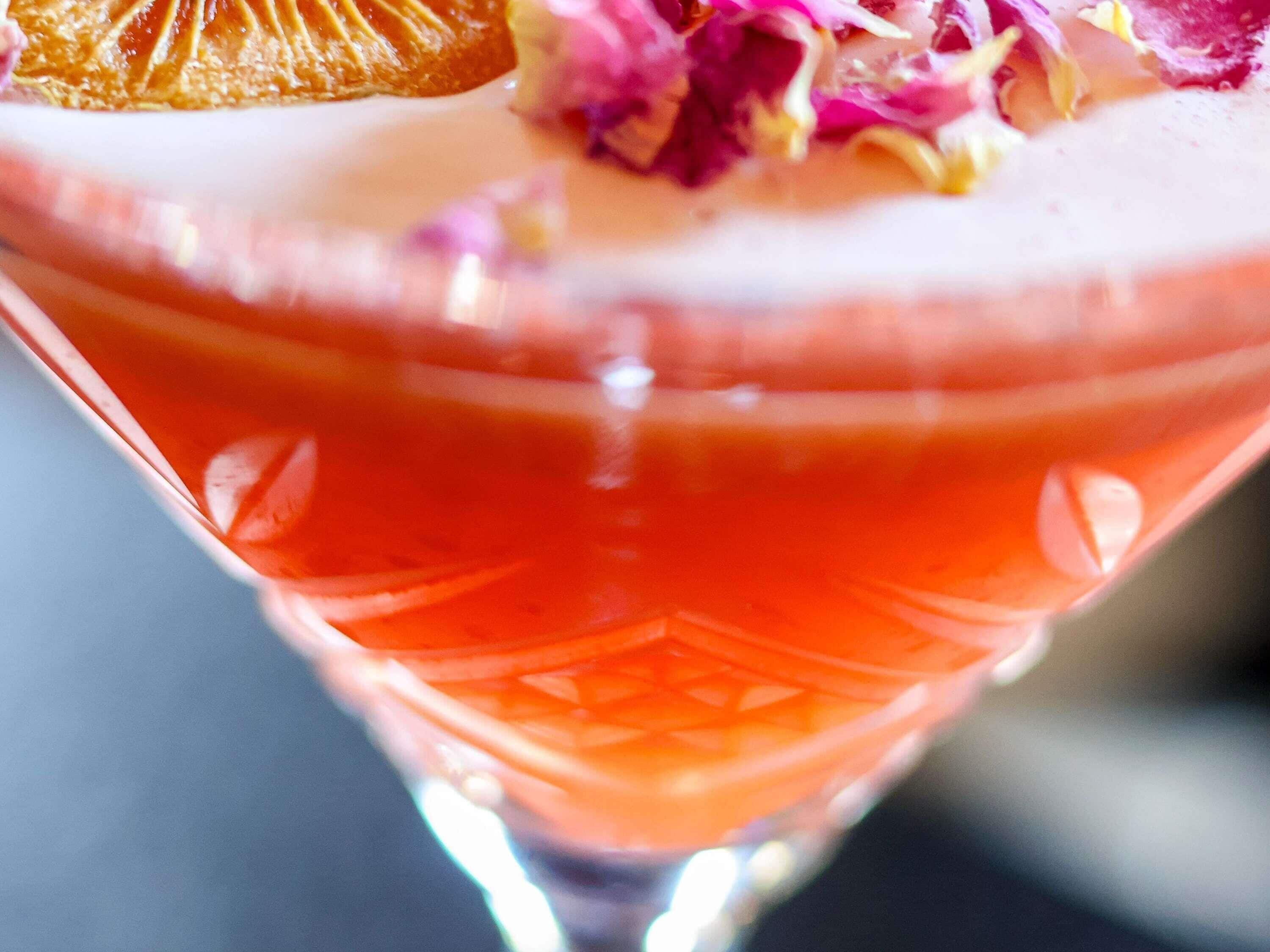Et nærbillede af en cocktail med lyserød farve og pyntet med lyserøde og lilla blomster.