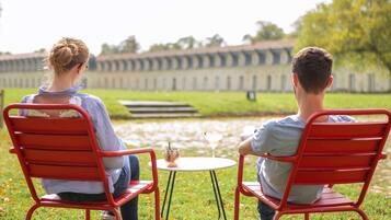 Guests can enjoy a tranquil outdoor setting with a table for two, surrounded by lush greenery and a serene water view.